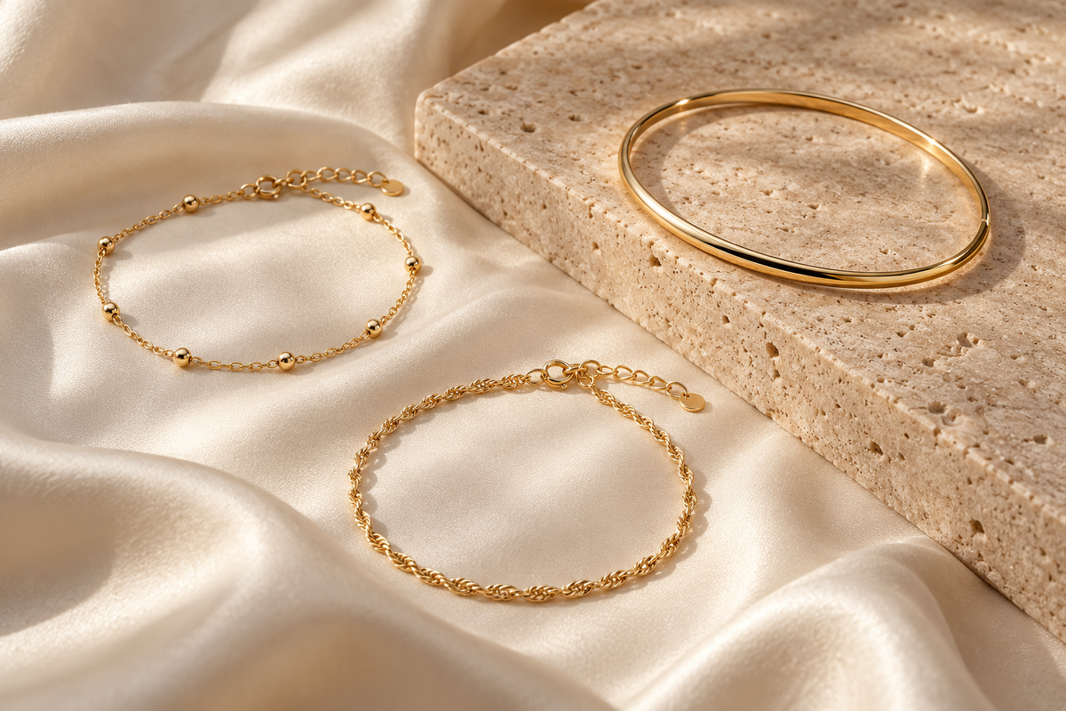 Editorial illustration of two gold chain bracelets and a slim bangle on ivory silk
